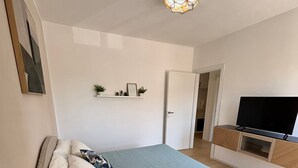 Een slaapkamer met een bed, nachtkastje, televisie en een deur naar een andere kamer.