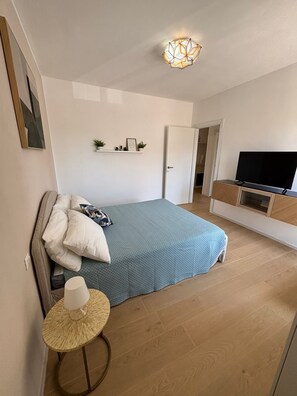 Ein Schlafzimmer mit Bett, Nachttisch, Fernseher und einer Tür zu einem anderen Raum.