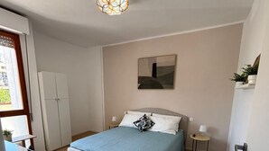 Een slaapkamer met een bed, nachtkastjes, een kledingkast, een plafondlamp en een schilderij aan de muur.