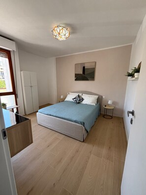 Ein Schlafzimmer mit einem Bett, Nachttischen, einem Kleiderschrank, einer Deckenleuchte und einem Bild an der Wand.