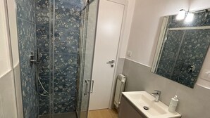 Een badkamer met een douchecabine van glas, een wit wastafelmeubel, een spiegel en een toilet.