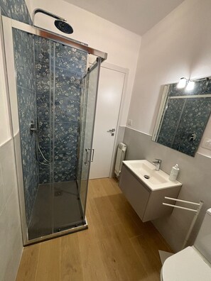 Ein Badezimmer mit Duschkabine, weißem Waschbecken, Spiegel und Toilette.