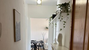 Een hal met een houten deur, een witte muur met een lijstwerk, een plafondlamp en een eethoek op de achtergrond.
