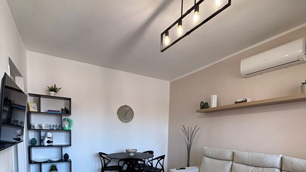 Een moderne woonkamer met een bank, eettafel, stoelen en een keuken met planken en apparatuur.
