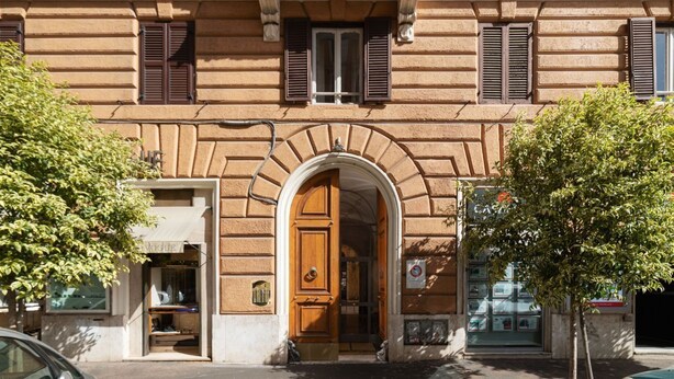 Fachada d'edifici amb un portal d'arc central, persianes a les finestres i una botiga amb un rètol.