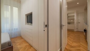 Habitació moderna amb televisió penjada a la paret, un armari i una cuina visible a través d'una porta oberta.