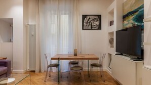 Un saló modern amb una taula de dinar de fusta, caires transparents, una taula de centre de vidre, un sofà, un televisor i obres d'art a les parets.