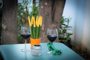 Zwei Weingläser auf einem Tisch, ein kleines Glas und ein Blumentopf mit gelben Blüten.