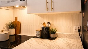 Una cucina moderna con mobili bianchi, un piano di lavoro nero e uno schienale in marmo.
