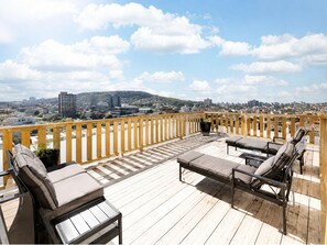 Eine Holzterrasse mit Sitzgelegenheiten und Blick auf die Stadt.