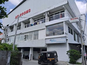A building with 'ACROOMS' signage, a 'Heaven Gardens' sign, and a parked auto-rickshaw. - Crest Wood Inn (Kanayannur)