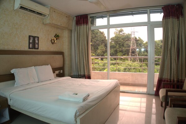 A hotel room with a large bed, a balcony with curtains, and a view of greenery. - Crest Wood Inn (Kanayannur)