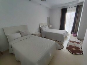 A hotel room with two beds, a nightstand, a mirror, and a window with curtains. - 2-bedroom apartment in marvelous Hurghada with AC and fitness room (Hurghada)