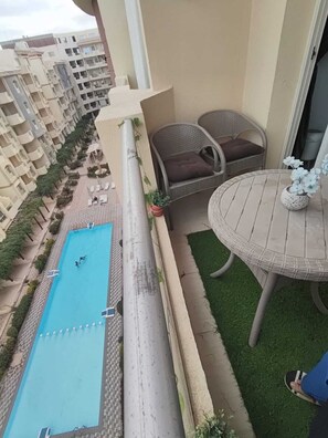 A balcony with a view of a swimming pool, a round table with chairs, and a potted plant. - 2-bedroom apartment in marvelous Hurghada with AC and fitness room (Hurghada)