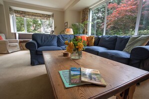 A living room with a sofa, a coffee table, and a window with a view of trees. - Wisteria Corner, Large Tranquil Family Home, Spacious, Edge of the Peak District (Chesterfield)