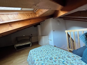 A bedroom with a sloped ceiling, a bed with a floral bedspread, a dresser, and a radiator. - Vrbo Property (Mastellina)