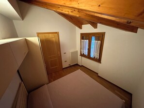 A room with a sloped ceiling, a wooden door, a radiator, and a window with lace curtains. - Vrbo Property (Mastellina)