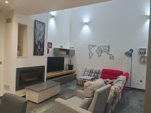 Un salon avec un téléviseur à écran plat, un canapé rouge, un fauteuil à motifs, une table basse et une carte du monde accrochée au mur.