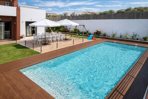 Una piscina rectangular con cubierta de madera, rodeada por una cerca blanca, y una pequeña zona de juegos con un tobogán.