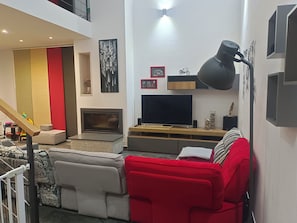 A modern living room with a flat-screen TV, a red sofa, and a staircase. - Villa Solaria Córdoba (Guadalcázar)