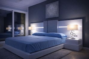 Un dormitorio moderno con una cama grande, dos mesitas de noche con lámparas, un espejo y una obra de arte colgada en la pared.