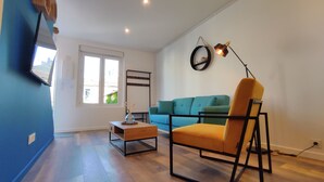 Uma sala de estar com sofá, poltrona, mesa de centro, televisão e abajur.
