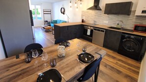 Uma cozinha moderna com área de jantar, piso de madeira, eletrodomésticos embutidos e vista para uma sala de estar.