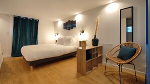 Quarto com cama, luminárias laterais, mesa de cabeceira, uma cadeira e espelho fixado na parede.
