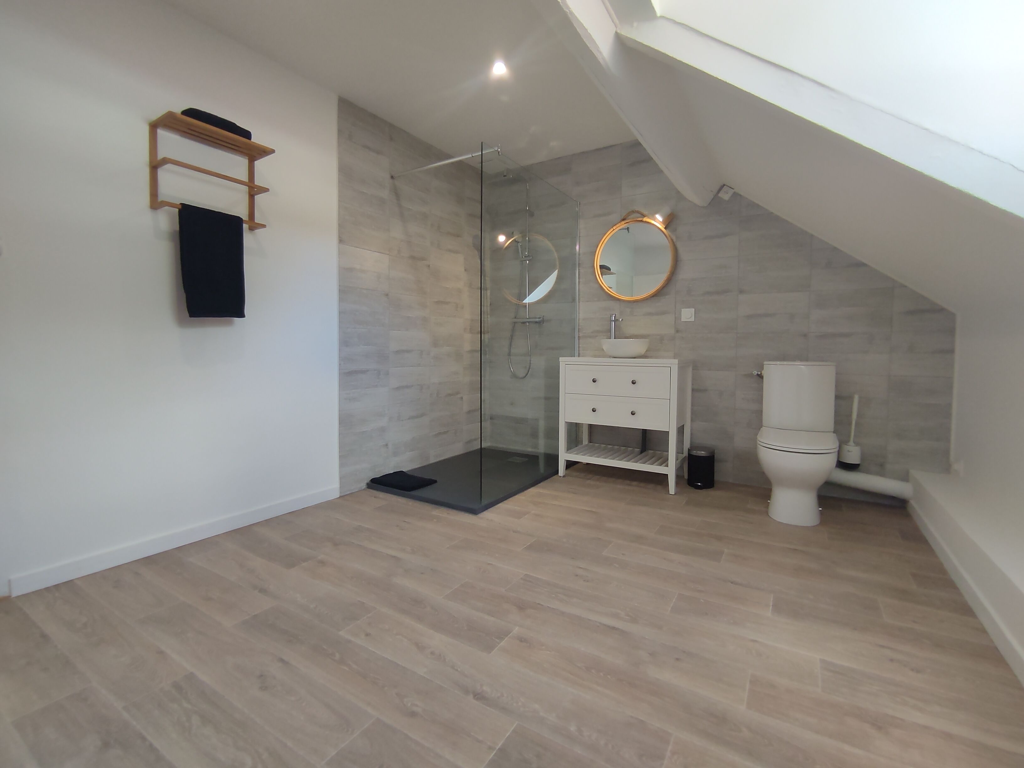 A modern bathroom with a glass shower enclosure, a white vanity with a round mirror, and a toilet.