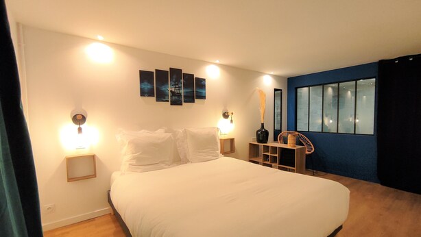 Quarto com uma cama grande, luminárias de cabeceira, mesa de cabeceira, um vaso e uma cadeira.