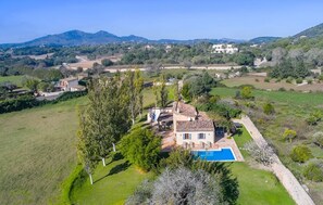 A villa with a swimming pool, surrounded by greenery and hills.