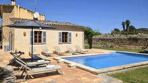 Eine Villa mit Swimmingpool, Sitzgelegenheit im Freien und einer Steinmauer.