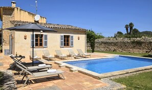 Een villa met een zwembad, terras en een stenen muur.