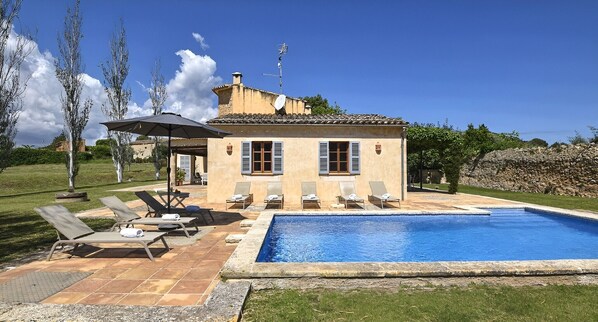 A villa with a swimming pool, outdoor seating, and a stone wall.
