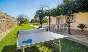 Une table de ping-pong avec une raquette, une piscine, des siĂšges dâextĂ©rieur et un mur en pierre.
