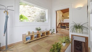Ein geräumiges Zimmer mit großem Fenster, Holzboden, einer eingebauten Pflanzenregal und einer Treppe zu einem weiteren Bereich.