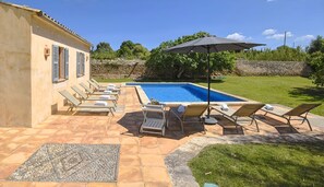 Un espace piscine aménagé avec des chaises longues, une pergola et un mur en pierre.