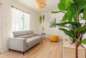 Een moderne woonkamer met een bank, een rond zitkussen, een lamp en een grote plant.