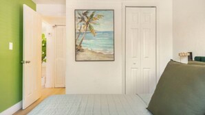 A bedroom with a bed, a door, a painting of a beach scene, and a green wall. - 4BR Home Near Wynwood + Huge Tropical Yard + BBQ (Miami)