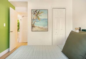 A bedroom with a bed, a door, a painting of a beach scene, and a green wall. - 4BR Home Near Wynwood + Huge Tropical Yard + BBQ (Miami)