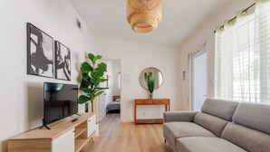A modern living room with a flat-screen TV, a grey sofa, a wooden coffee table, and a large green plant. - 4BR Home Near Wynwood + Huge Tropical Yard + BBQ (Miami)