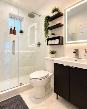 Un bagno moderno con cabina doccia in vetro, un WC, un mobile lavabo con specchio e mensole con piante e articoli da toilette.
