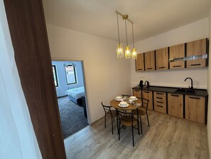 A modern kitchen with wooden cabinets, a dining table set for four, and a hanging light fixture. - Random Studio | Pet-Friendly Stay | Cozy Apartment (Brașov)