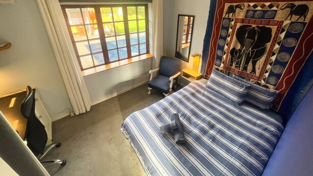 Ein Hotelzimmer mit Bett, Stuhl, Schreibtisch, einem Fenster mit Vorhängen und Wandteppich.