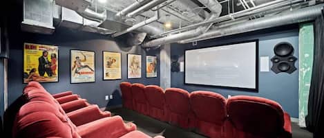 Une salle de cinéma avec des sièges rouges, un écran de projection et des affiches aux murs.