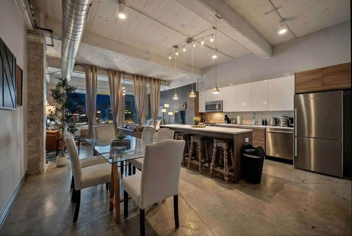 A modern kitchen with stainless steel appliances, a dining area with a glass table, and a view of the city at night.