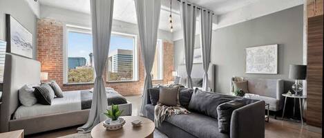 Una sala de estar moderna con un sofá gris, una mesa de centro redonda y vistas de la ciudad a través de amplias ventanas.