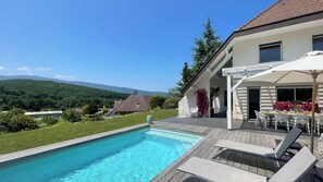 Ein Schwimmbecken mit Holzterrasse, Sitzgelegenheiten im Freien und Blick auf Berge.