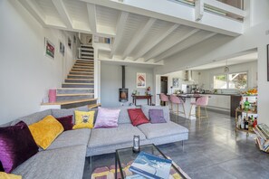 Ein großzügiger Wohnbereich mit grauem Sofa, einer Treppe, einer Küche und einer Bar.