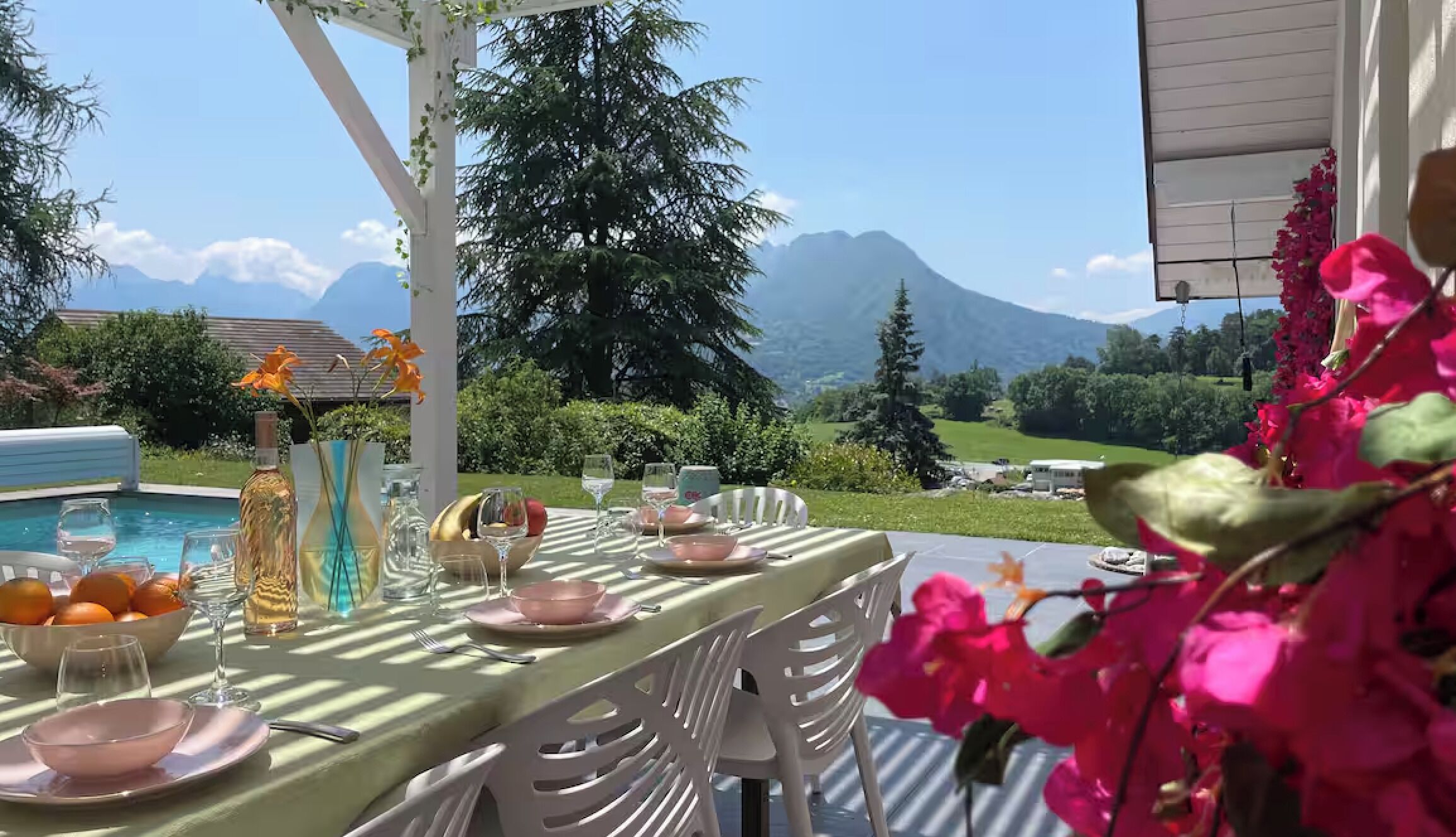 Ett utomhusområde med plats för måltider, med utsikt över berg, en pool och en vit pergola.